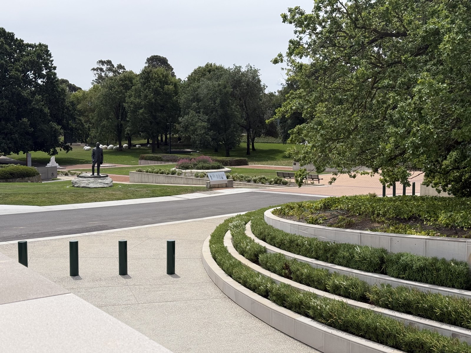 A curved limestone bench in the Sculpture Garden engraved with lines from In Flanders Fields, with pink salvia flowering and the marble droplets visible behind.